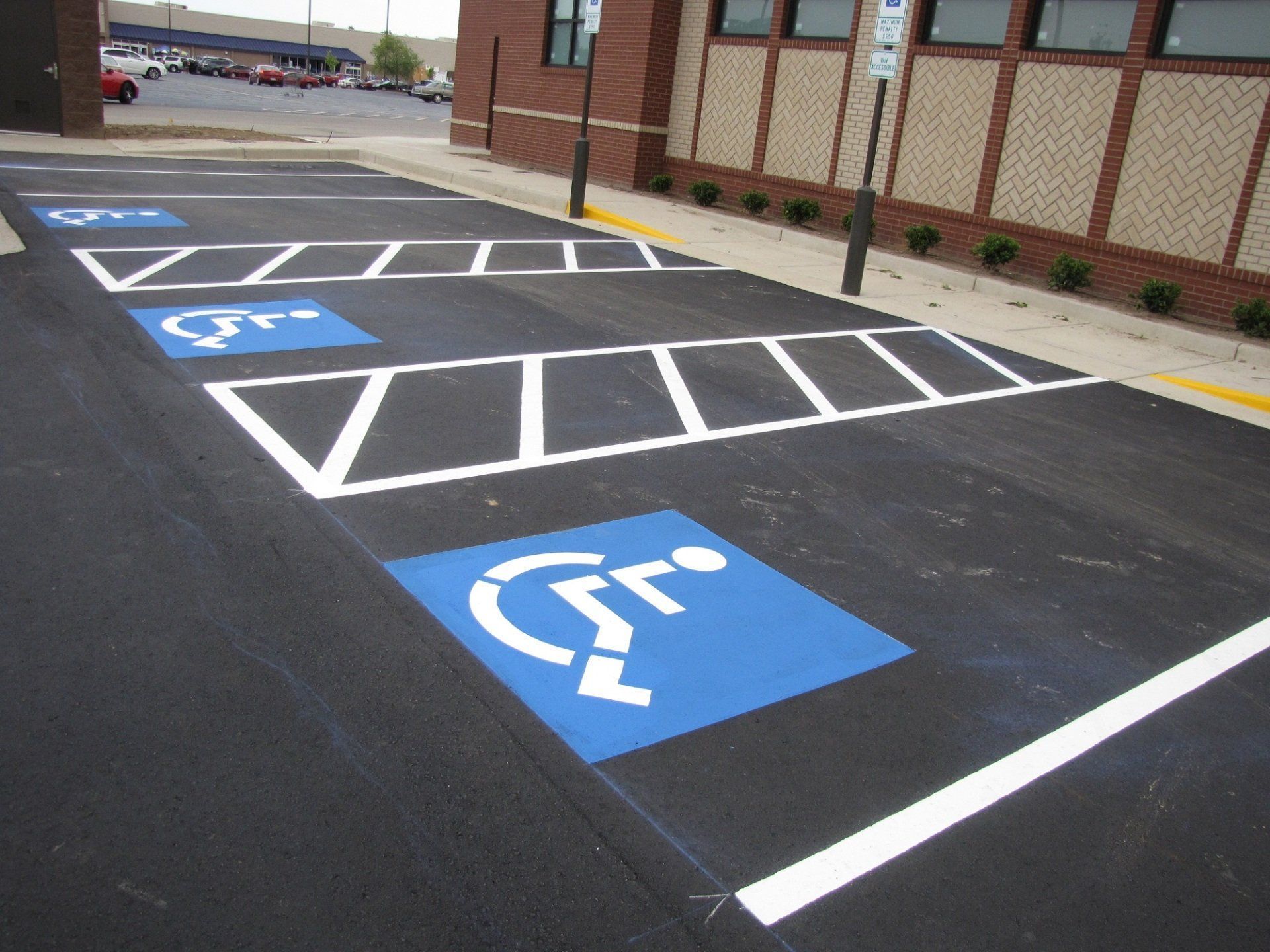 A freshly painted parking lot with multiple blue and white wheelchair-accessible parking symbols and safety hash markings.