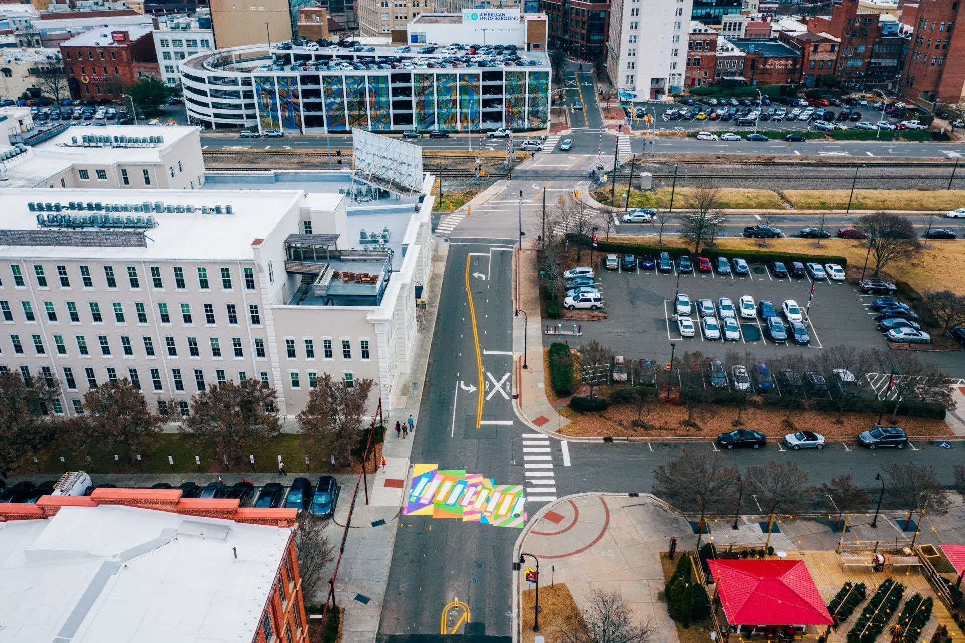 Aerial view of a city street featuring a vibrant, multi-colored mural on the pavement near a large white office building.