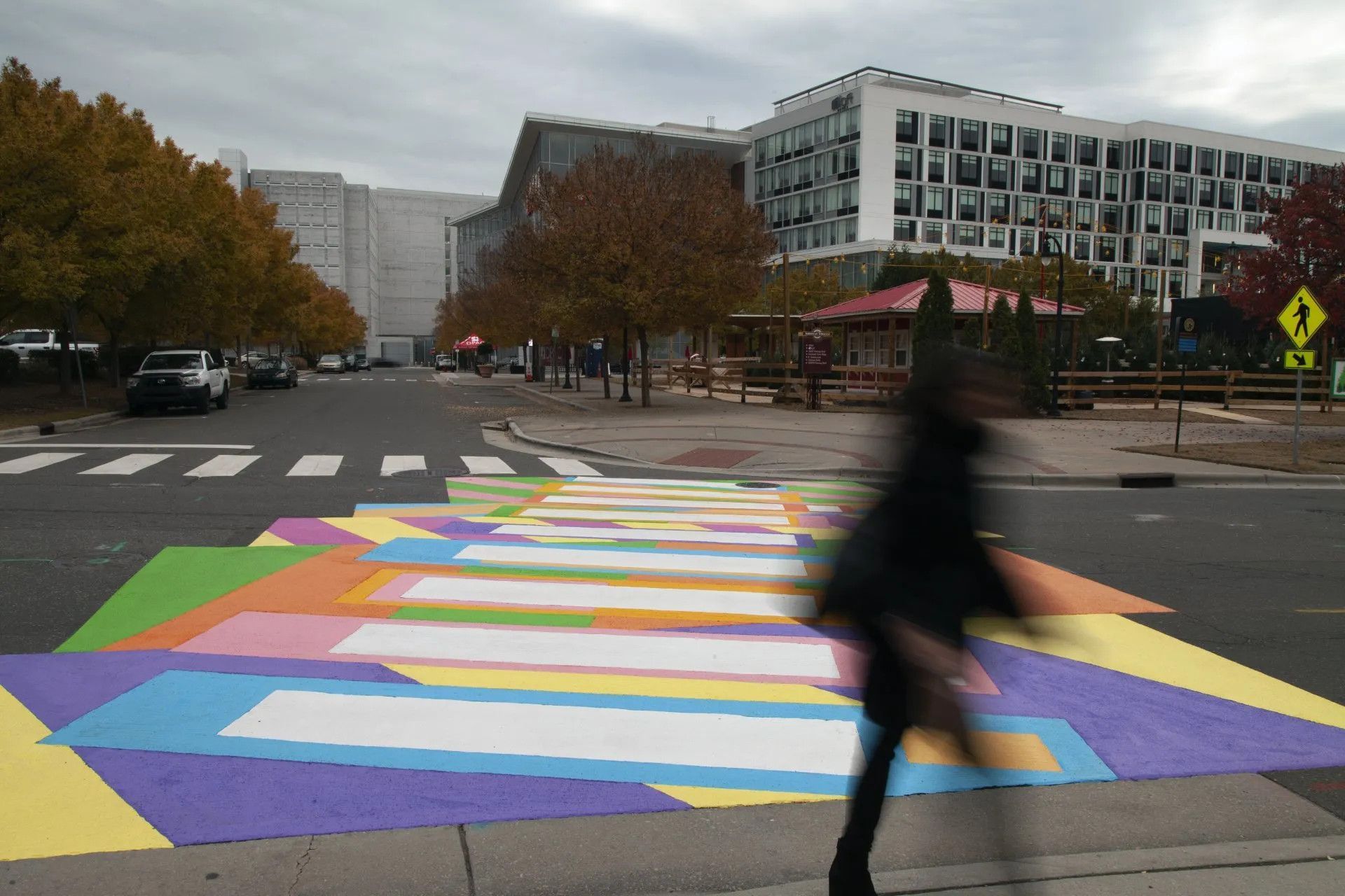 A colorful, geometric mural painted across a crosswalk on an asphalt road with a blurred person walking across it.