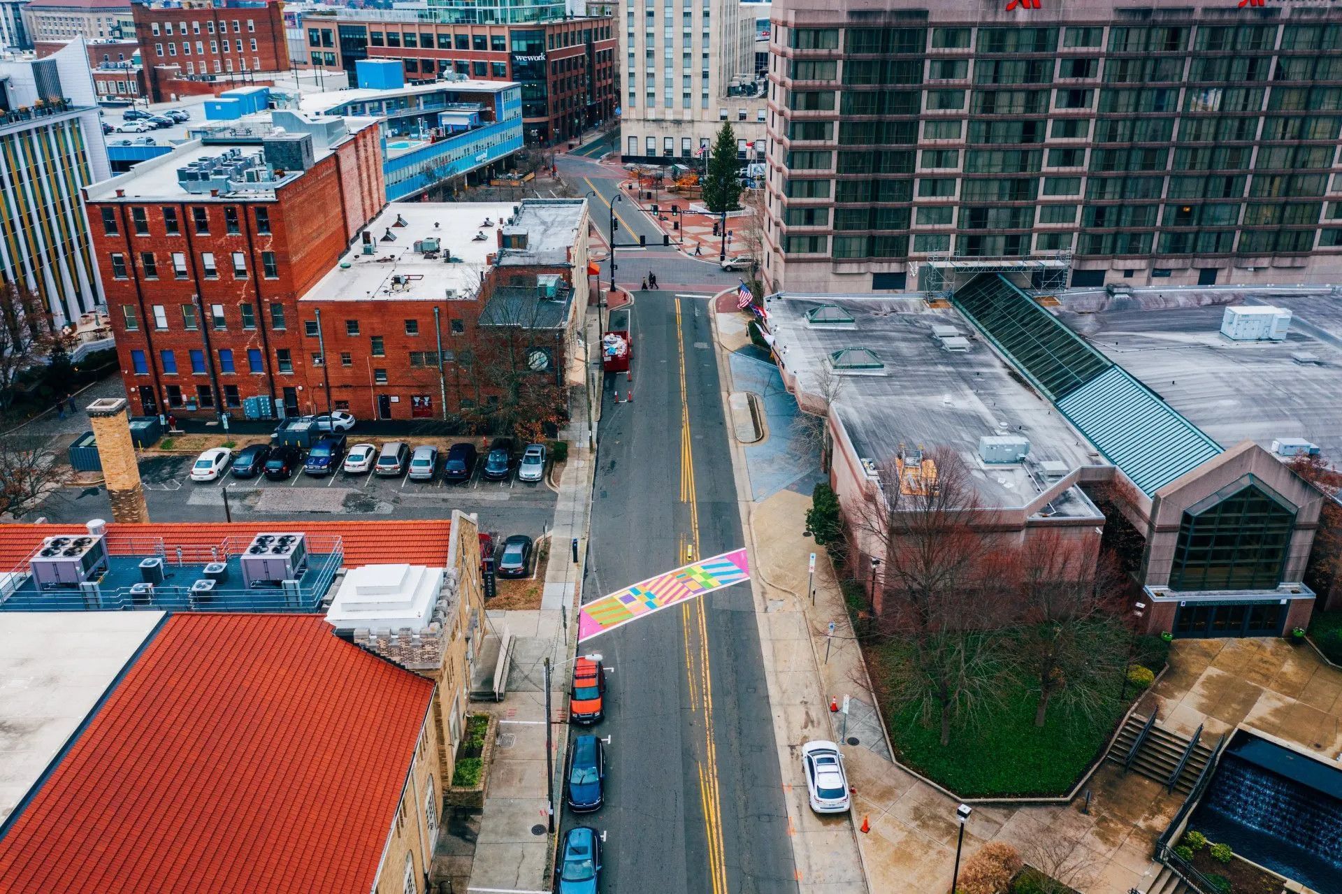 Aerial view of a city street featuring a multi-colored crosswalk mural painted on the asphalt.