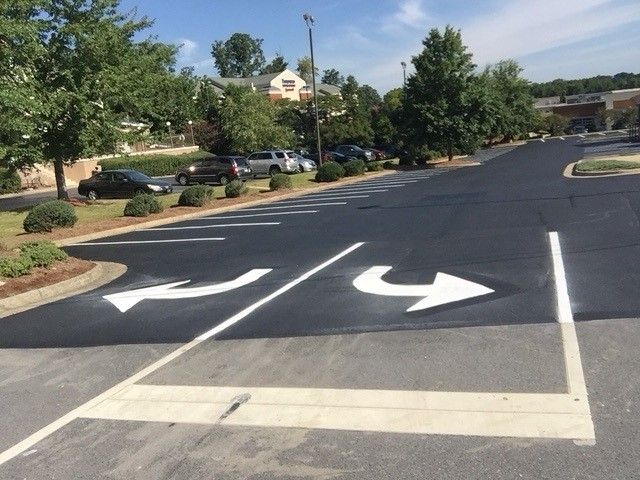 Parking lot lane with white directional arrows painted on dark asphalt near trees and buildings