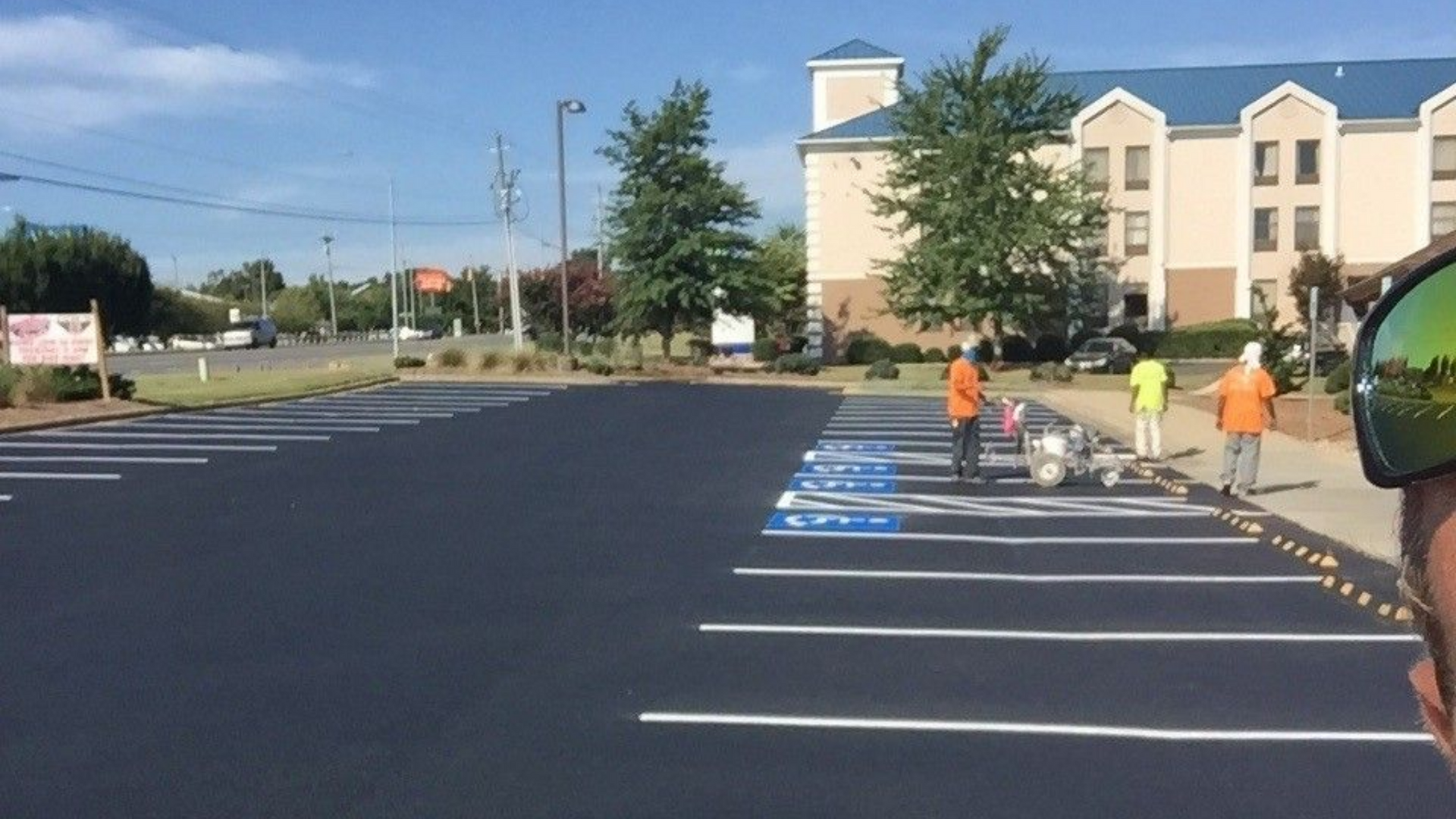 Parking lot with painted parking spaces and workers in orange and yellow vests near a building.