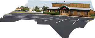 A wooden building with a green-trimmed entrance and a large, empty asphalt parking lot with white painted lines.