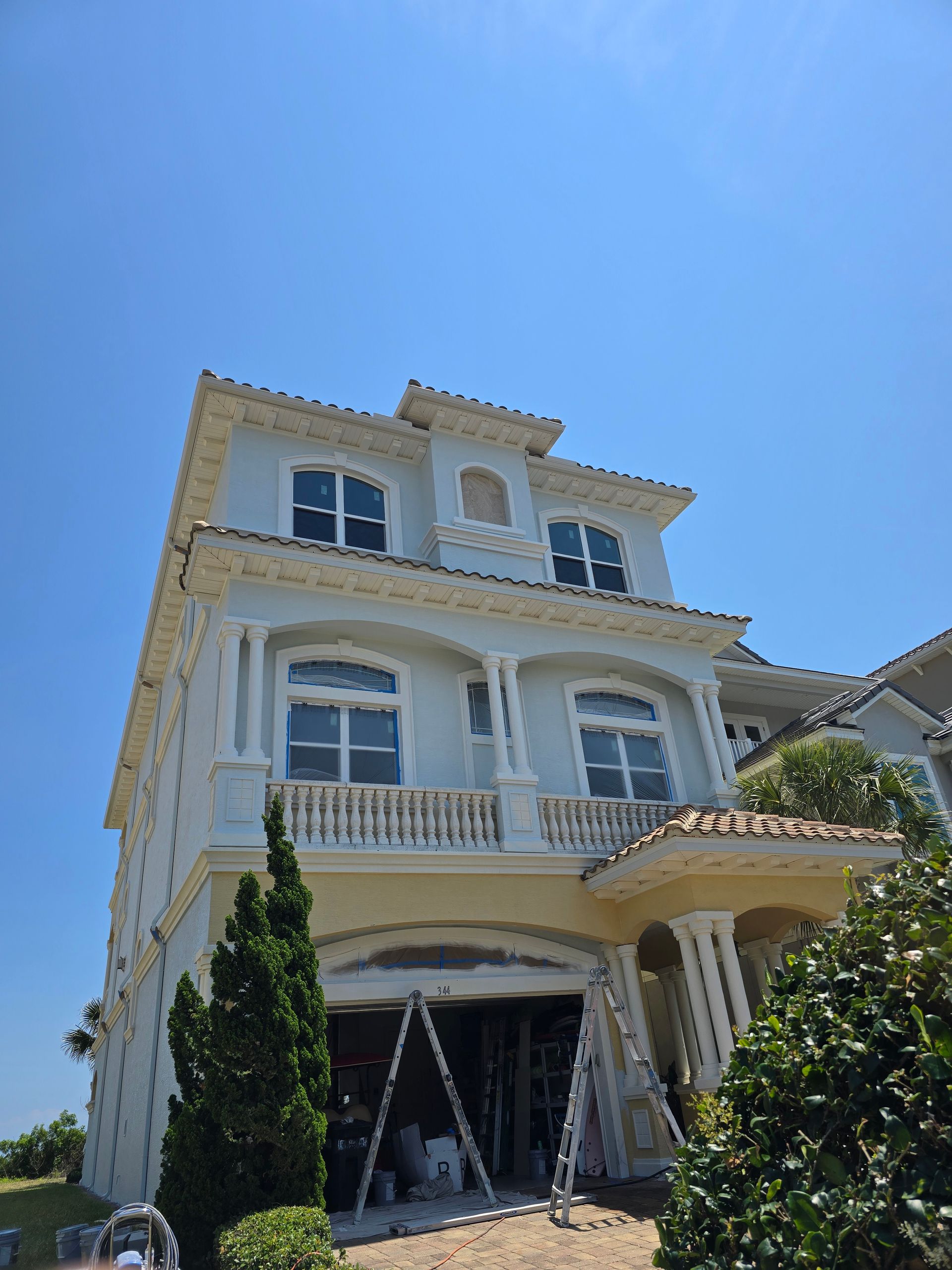 A large white house is being painted on a sunny day.