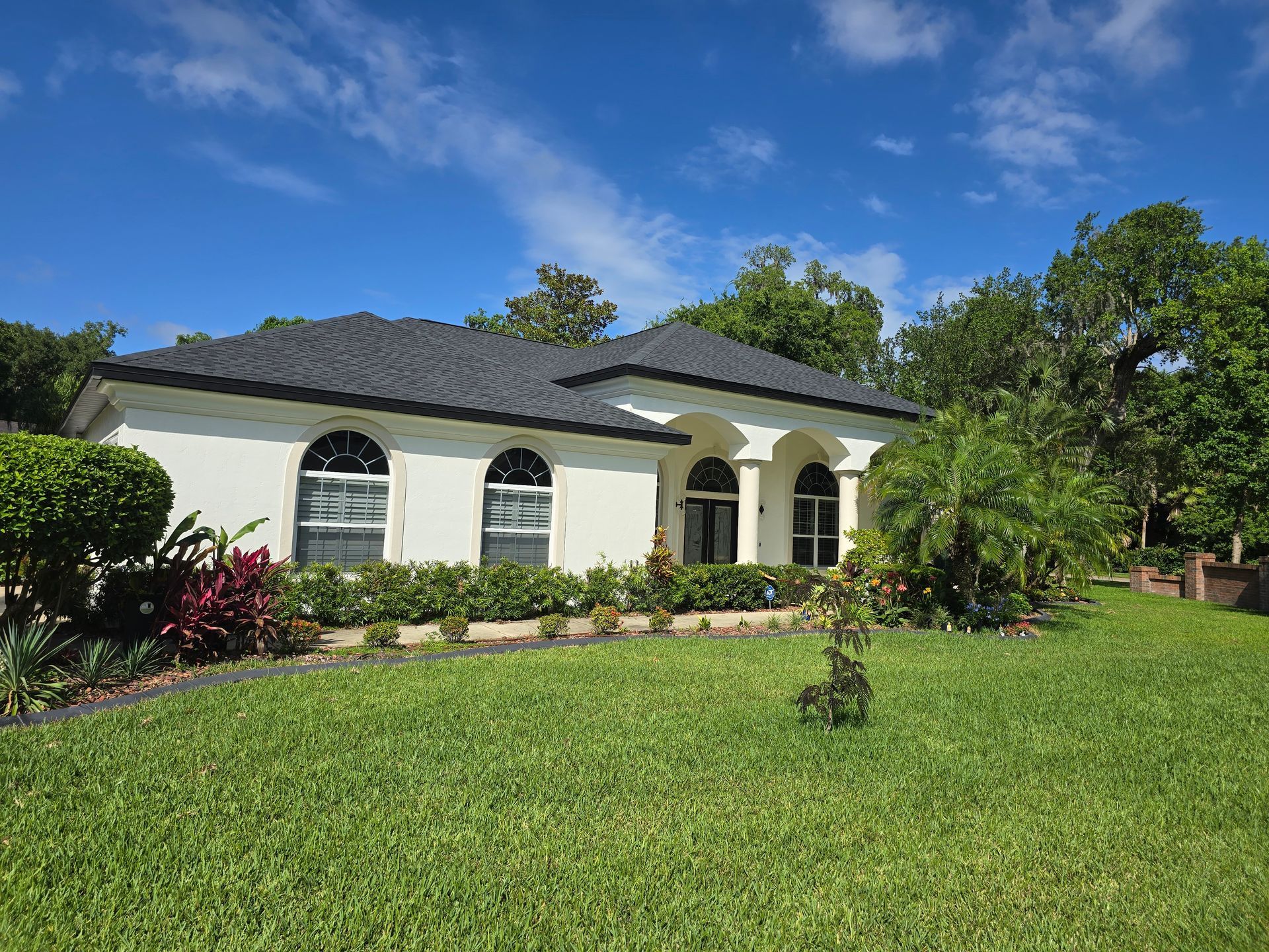 A white house with a black roof and a lush green lawn in front of it.
