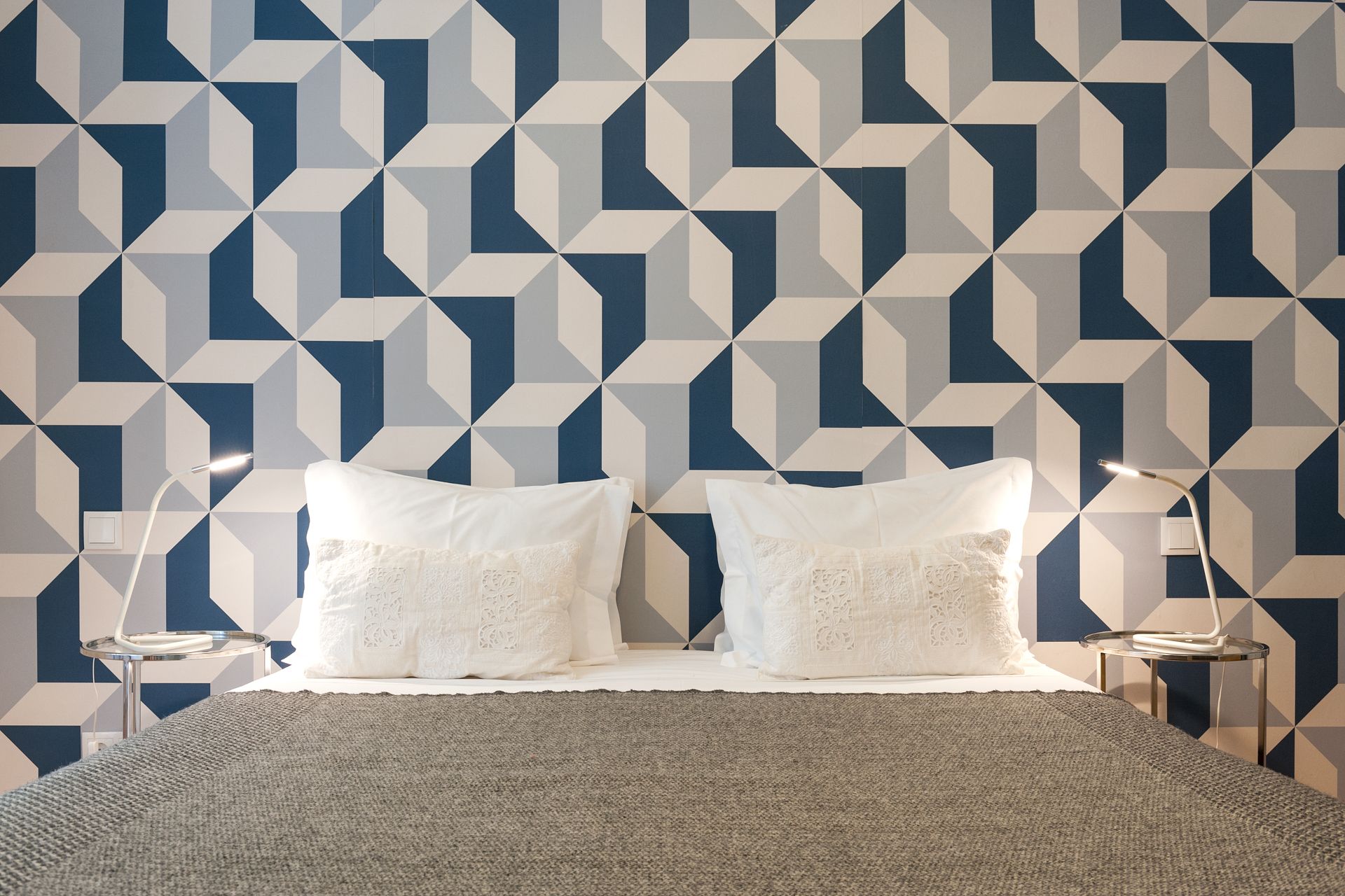 A bed in front of a wall with a geometric pattern. Cheese & Wine Suites.