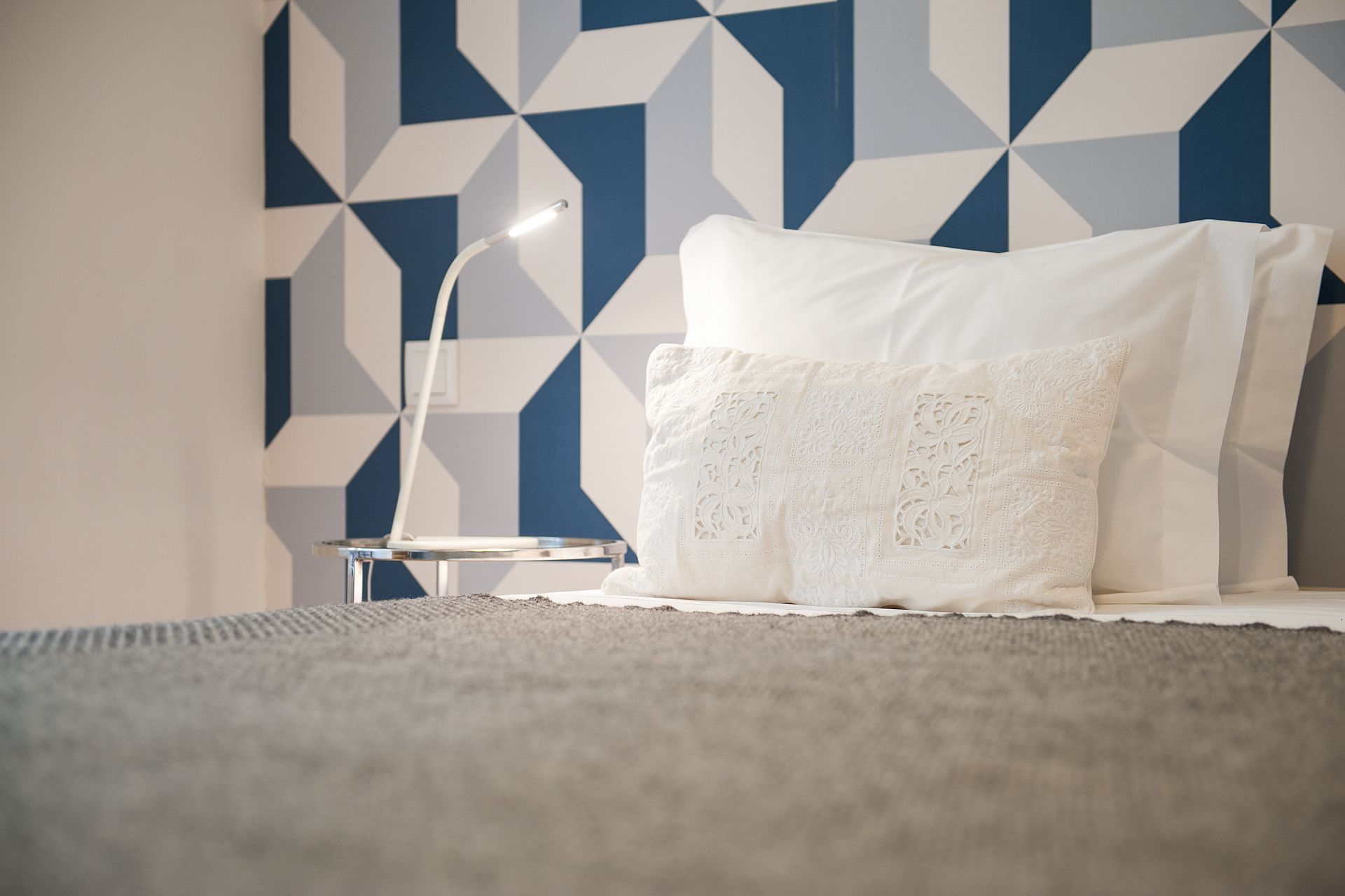 A bed with a blue and white patterned wall behind it. Cheese & Wine Suites.