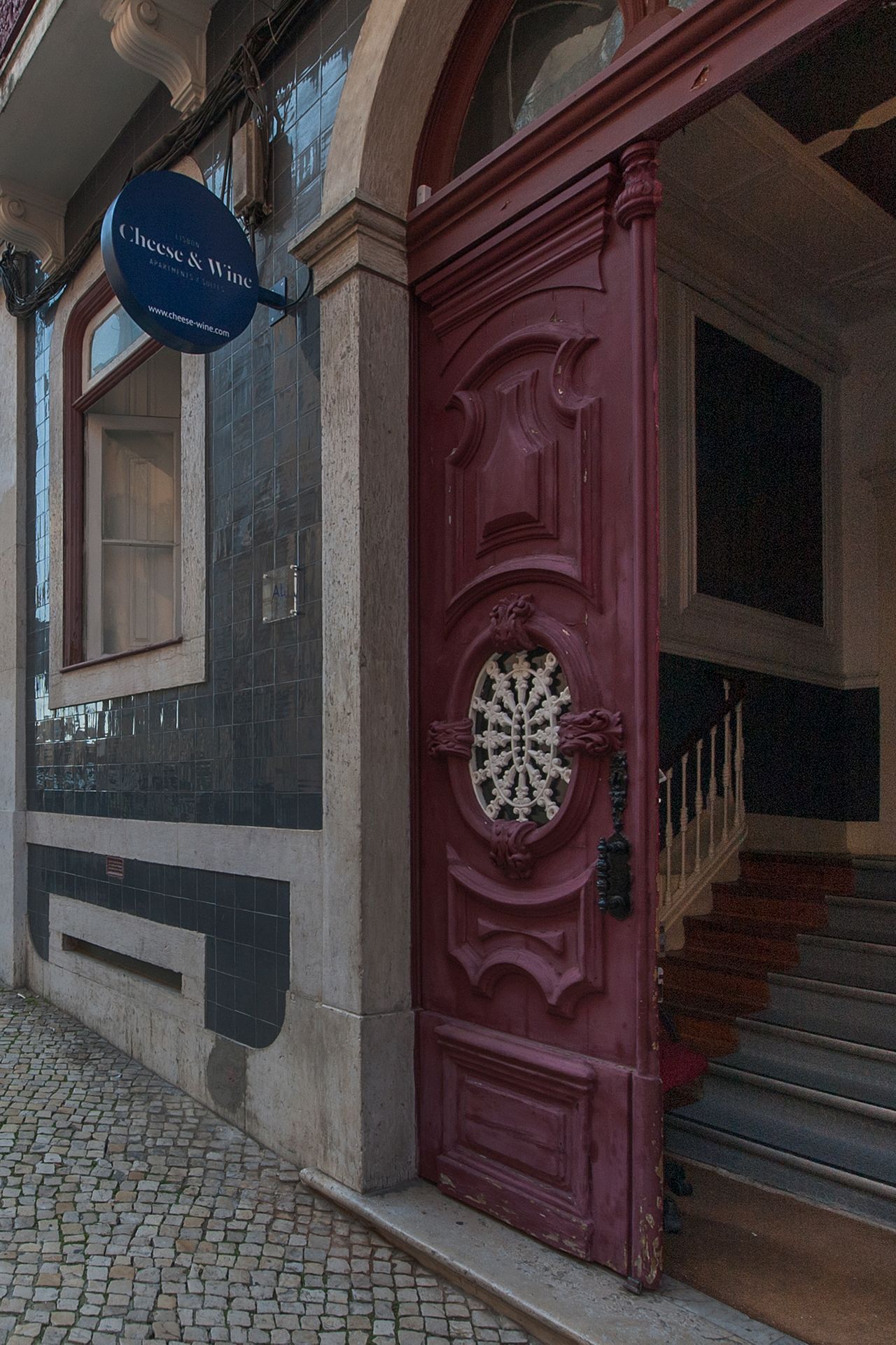 The Cheese & Wine Suites building with a red door and stairs in front of it.