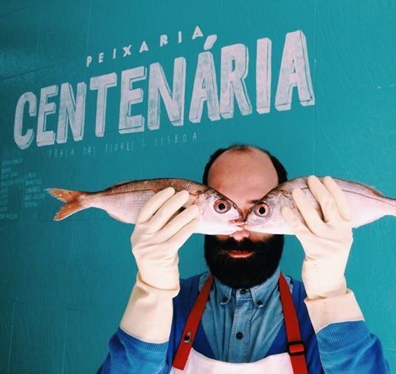 A man holding two fish in front of his face in front of a sign of the Fishmonger