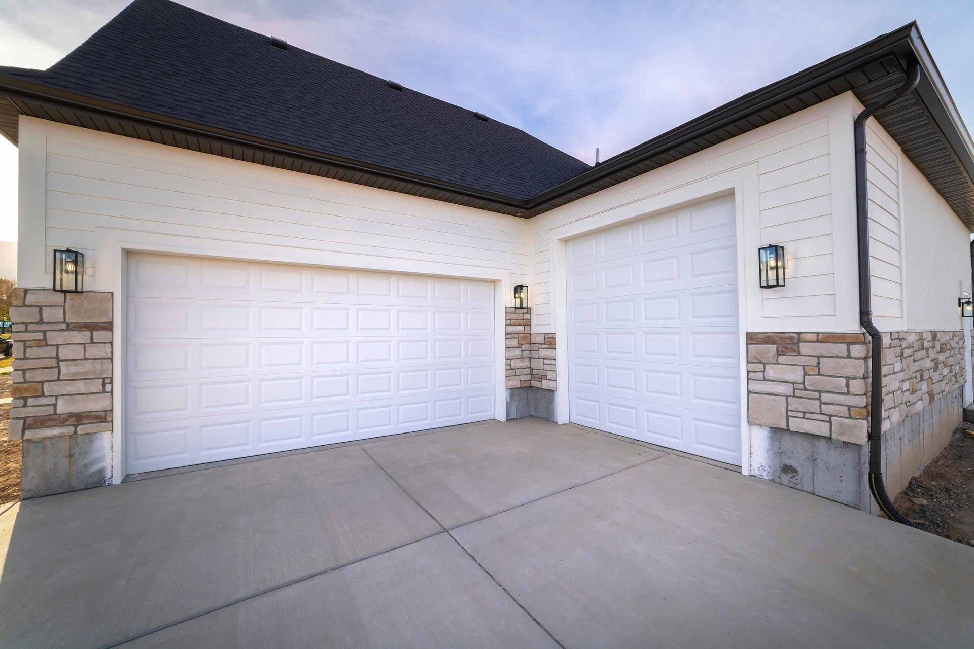 Two-car garage with white doors, stone trim, and a concrete driveway under a dark roof.