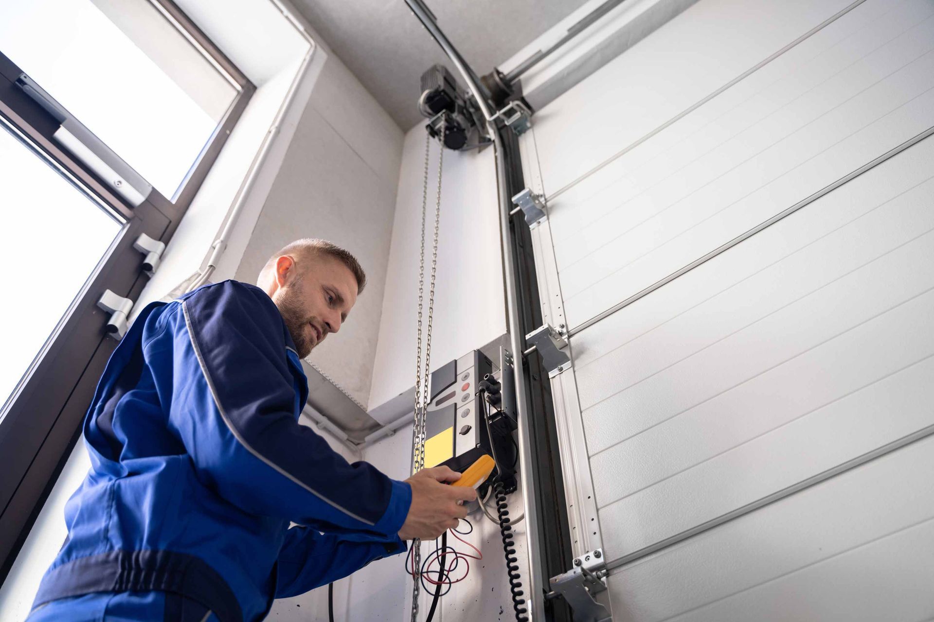 Worker operating a yellow controller beside a large industrial garage door