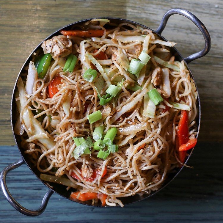 A pan filled with noodles and vegetables on a wooden table.
