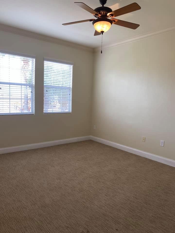 An empty room with a ceiling fan and two windows