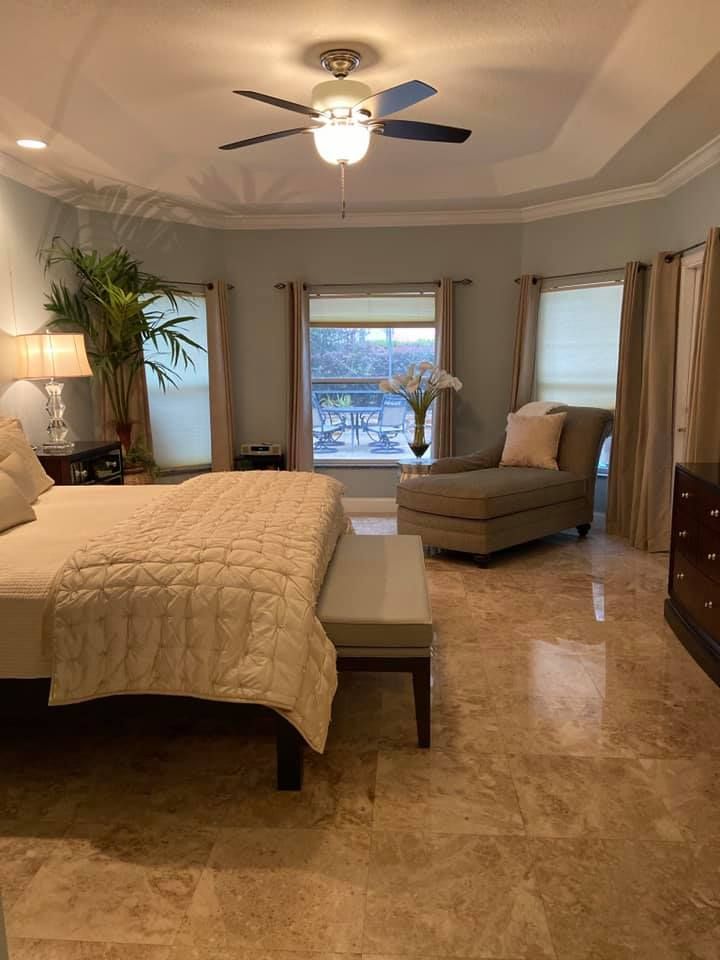 A bedroom with a bed , chair , bench and ceiling fan.