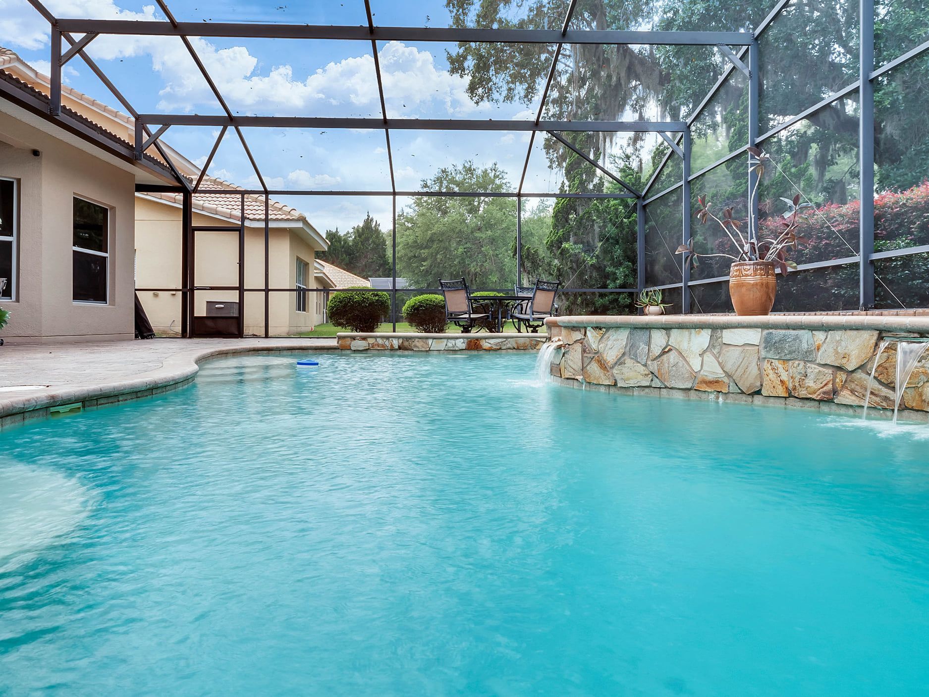 A large swimming pool with a waterfall in the backyard of a house.