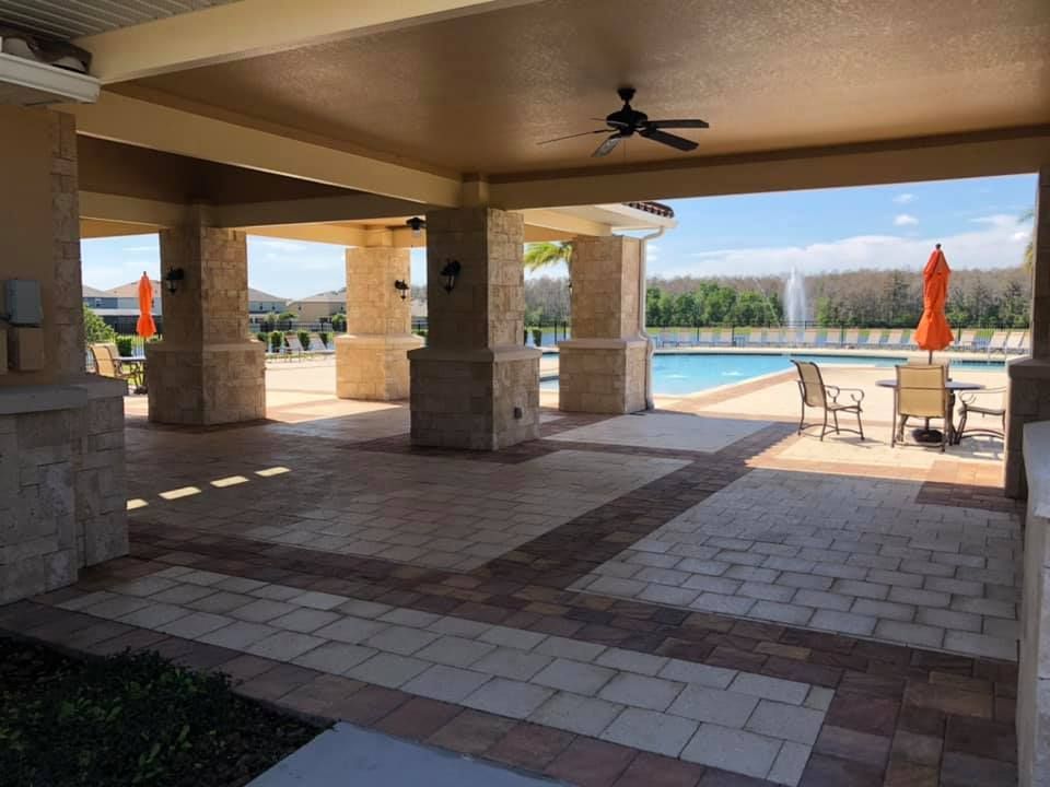 A patio with tables and chairs and a ceiling fan overlooking a pool.