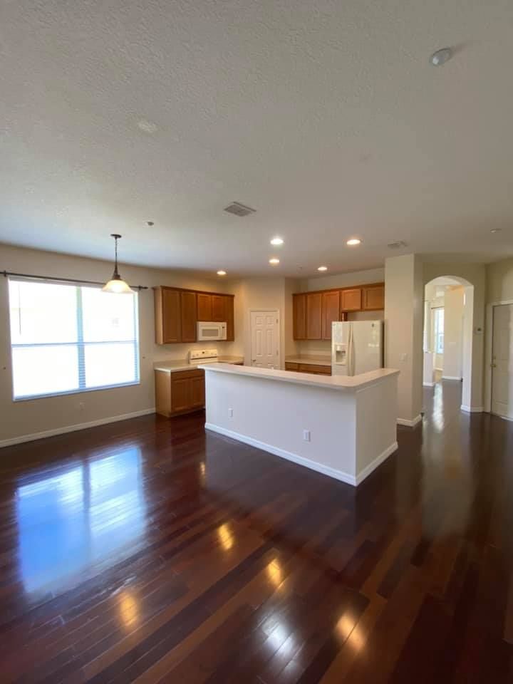 An empty living room with hardwood floors and a kitchen.