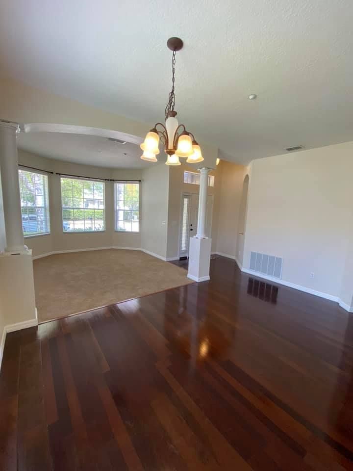 An empty living room with hardwood floors and a chandelier hanging from the ceiling.