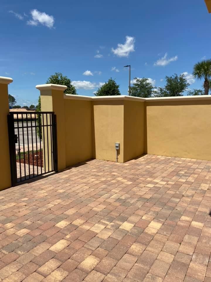 A brick driveway with a yellow wall and a gate