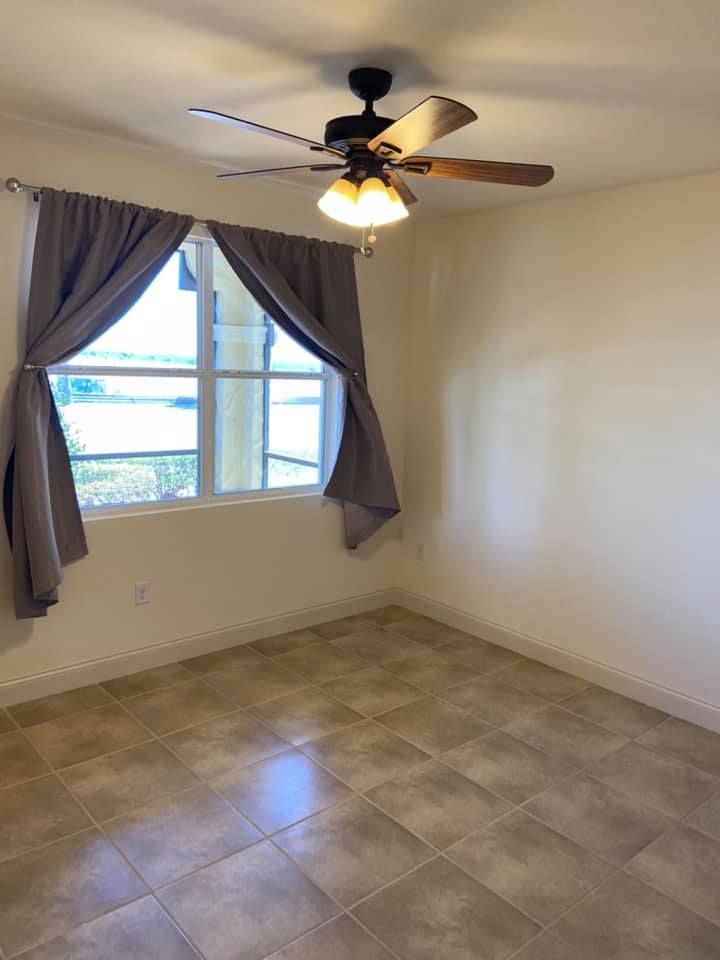 An empty room with a ceiling fan and a window.