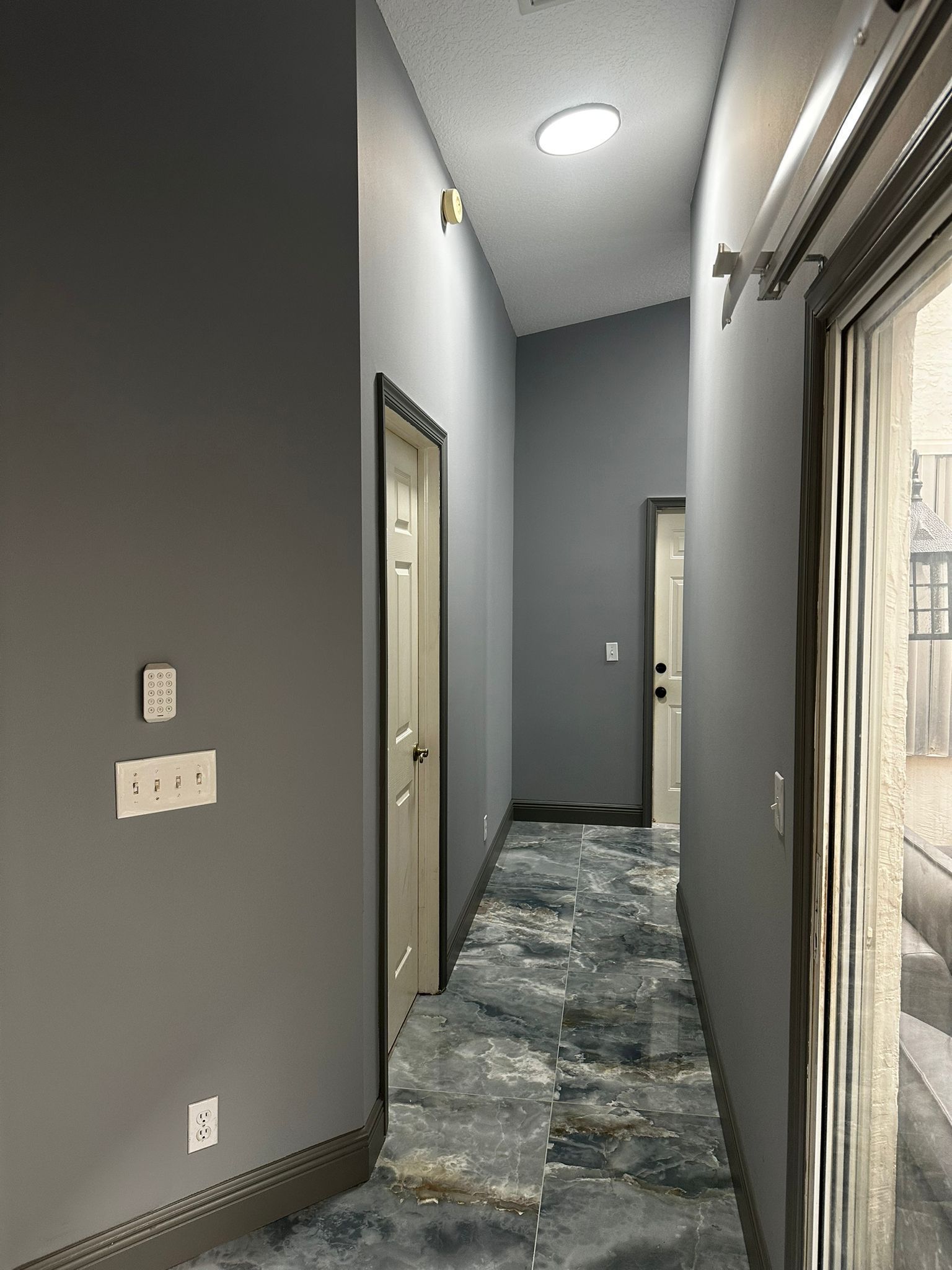 A long hallway in Martin County, FL with gray walls and a tiled floor leading to a door.