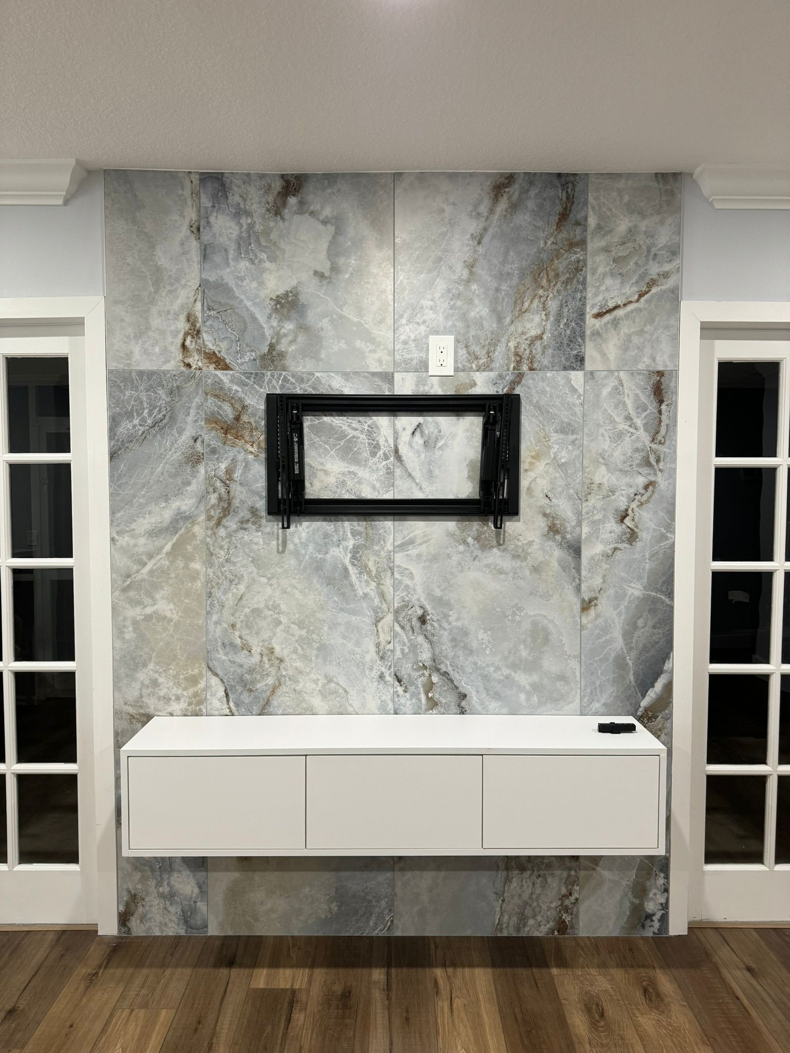 A living room  in Palm Beach County with a marble wall and a flat screen tv mounted on it.