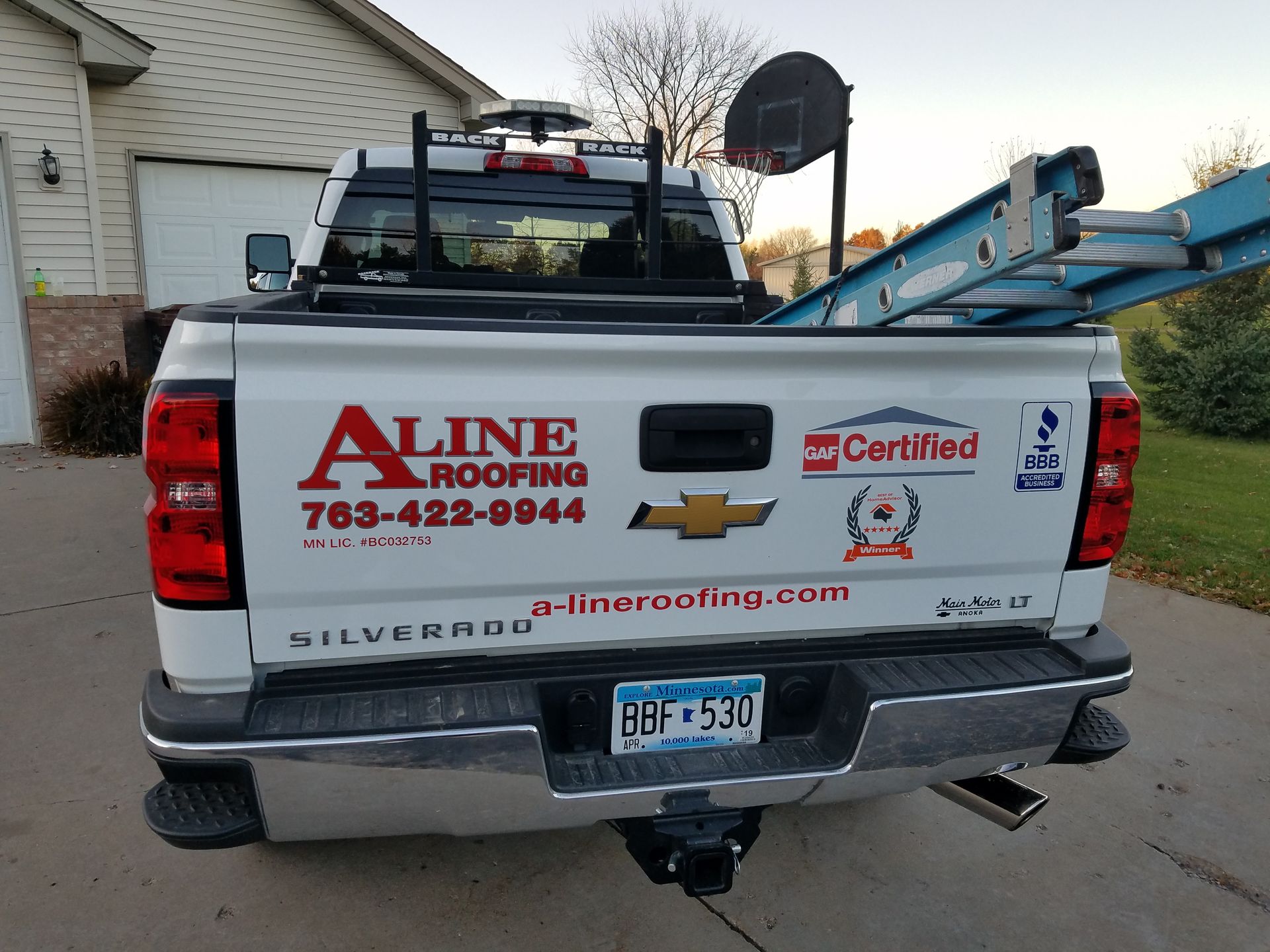 A line roofing truck is parked in front of a house