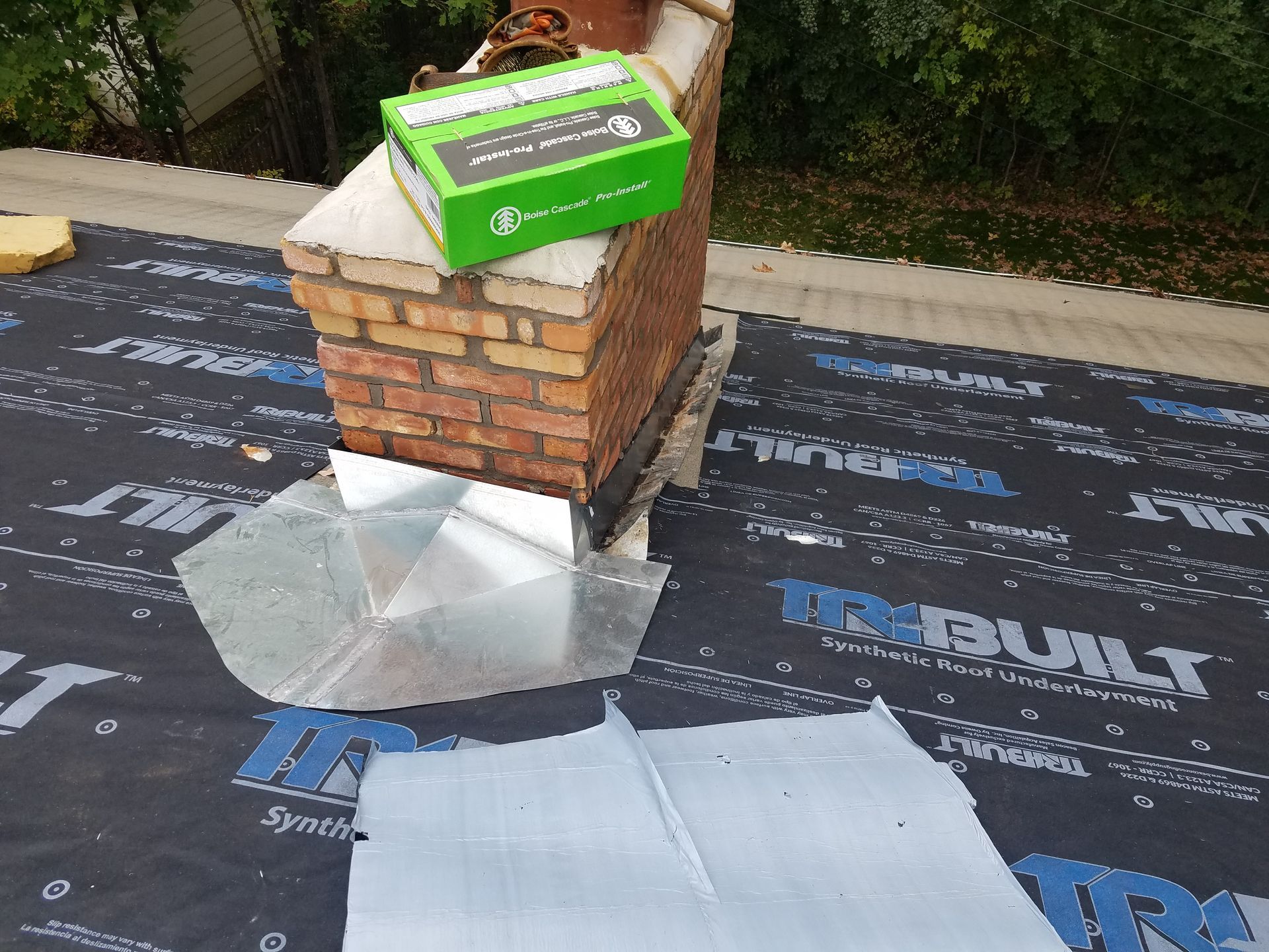 A brick chimney is sitting on top of a black tarp on a roof.