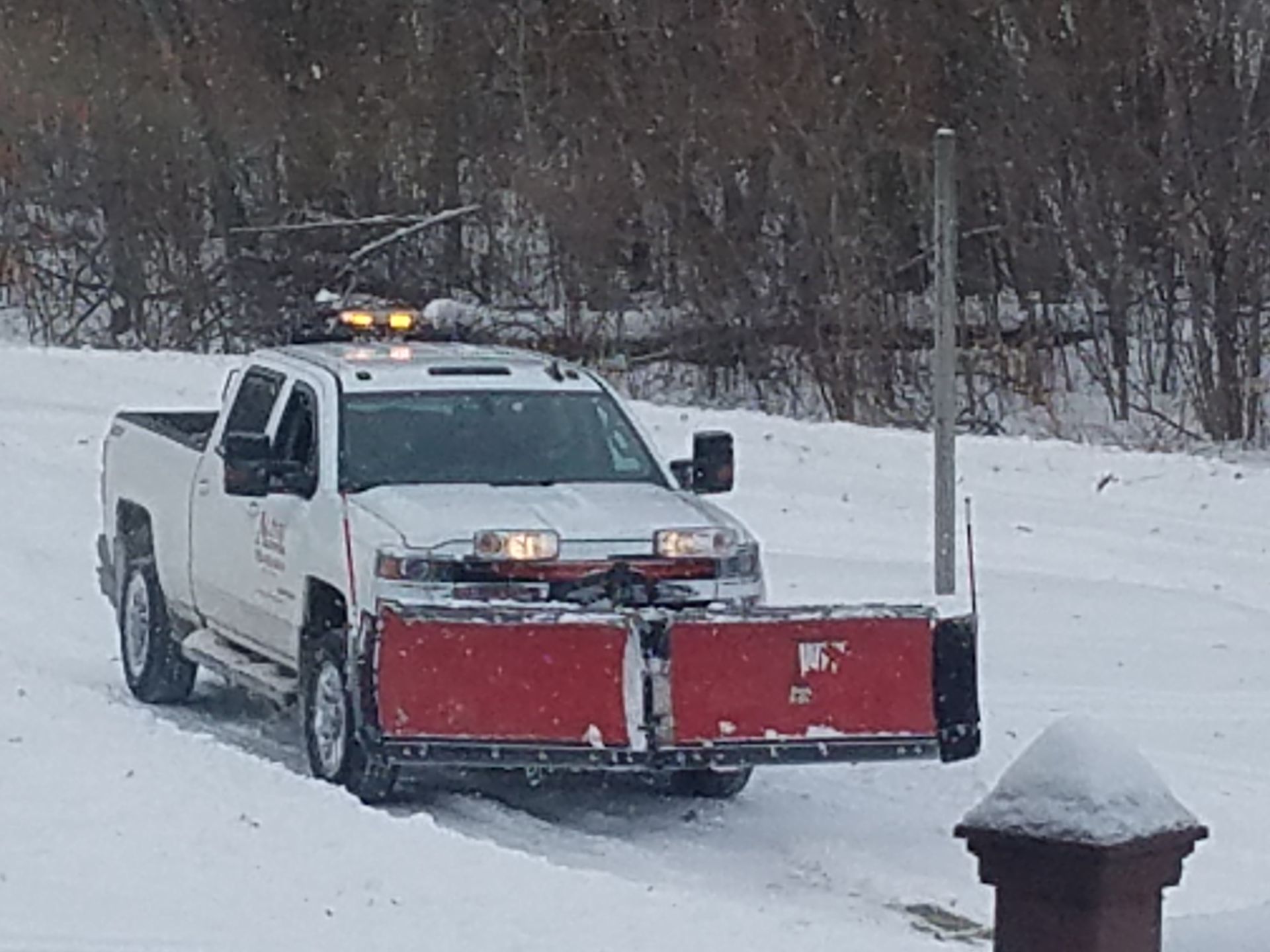 A white truck with a red plow on the back is driving down a snowy road.