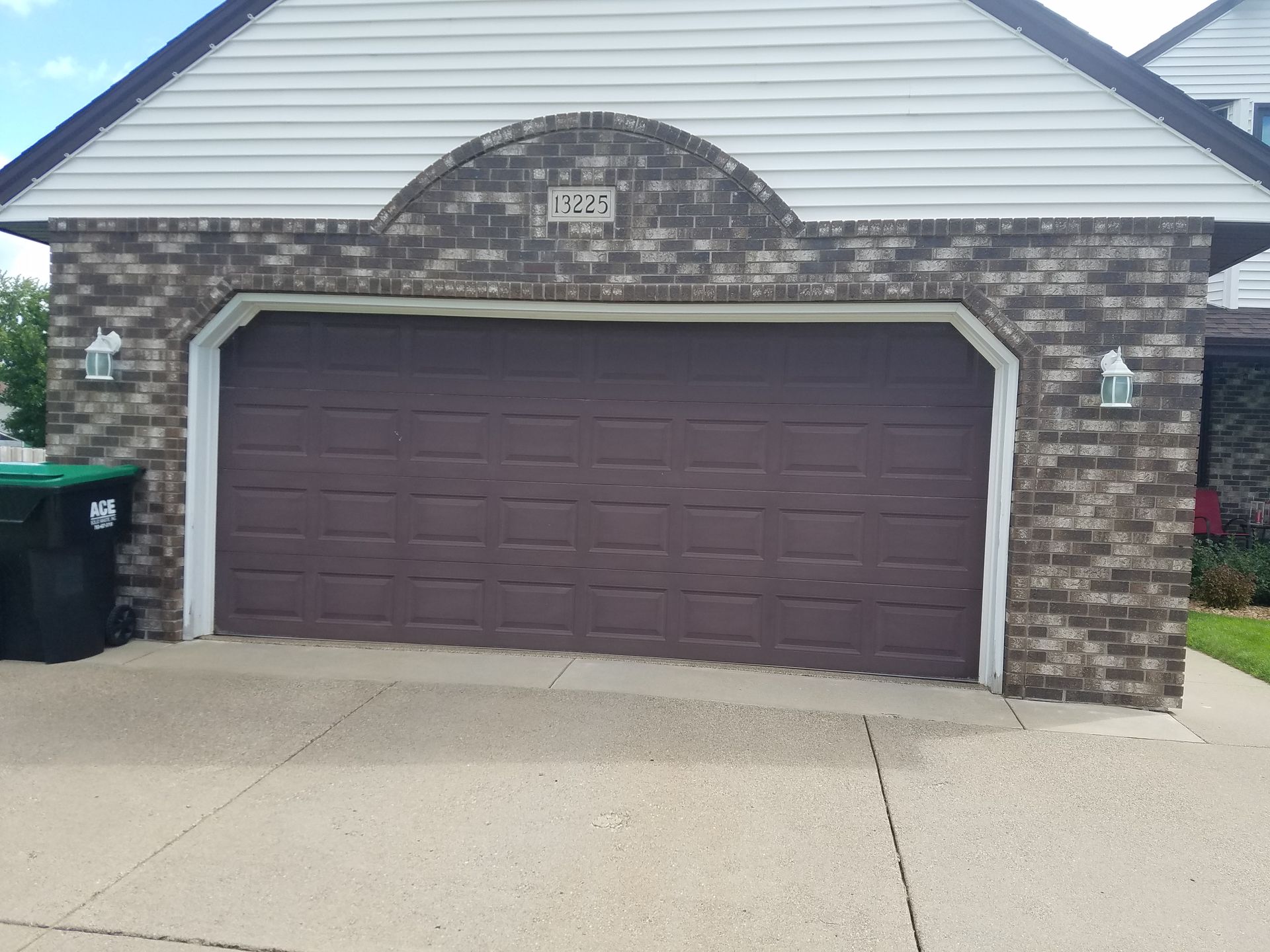 A brick house with a purple garage door and a green trash can in front of it.