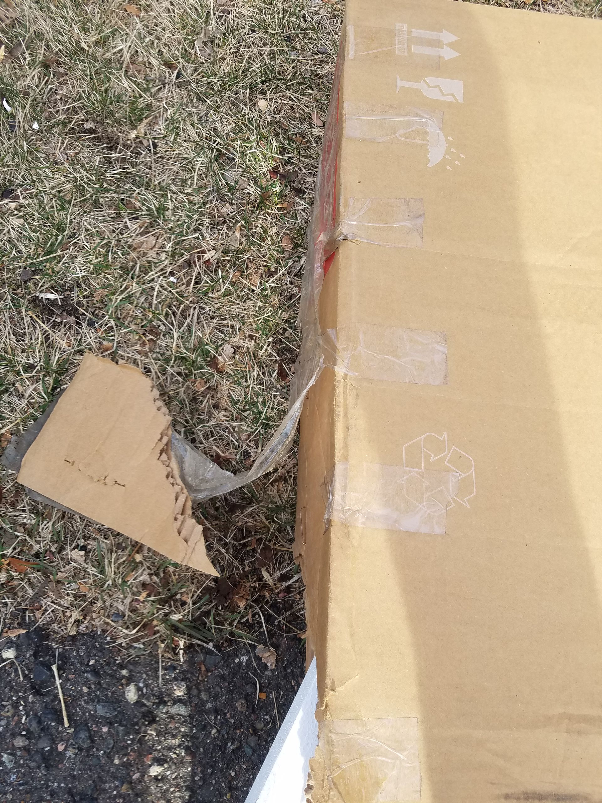 A cardboard box with tape on it is sitting on the ground.