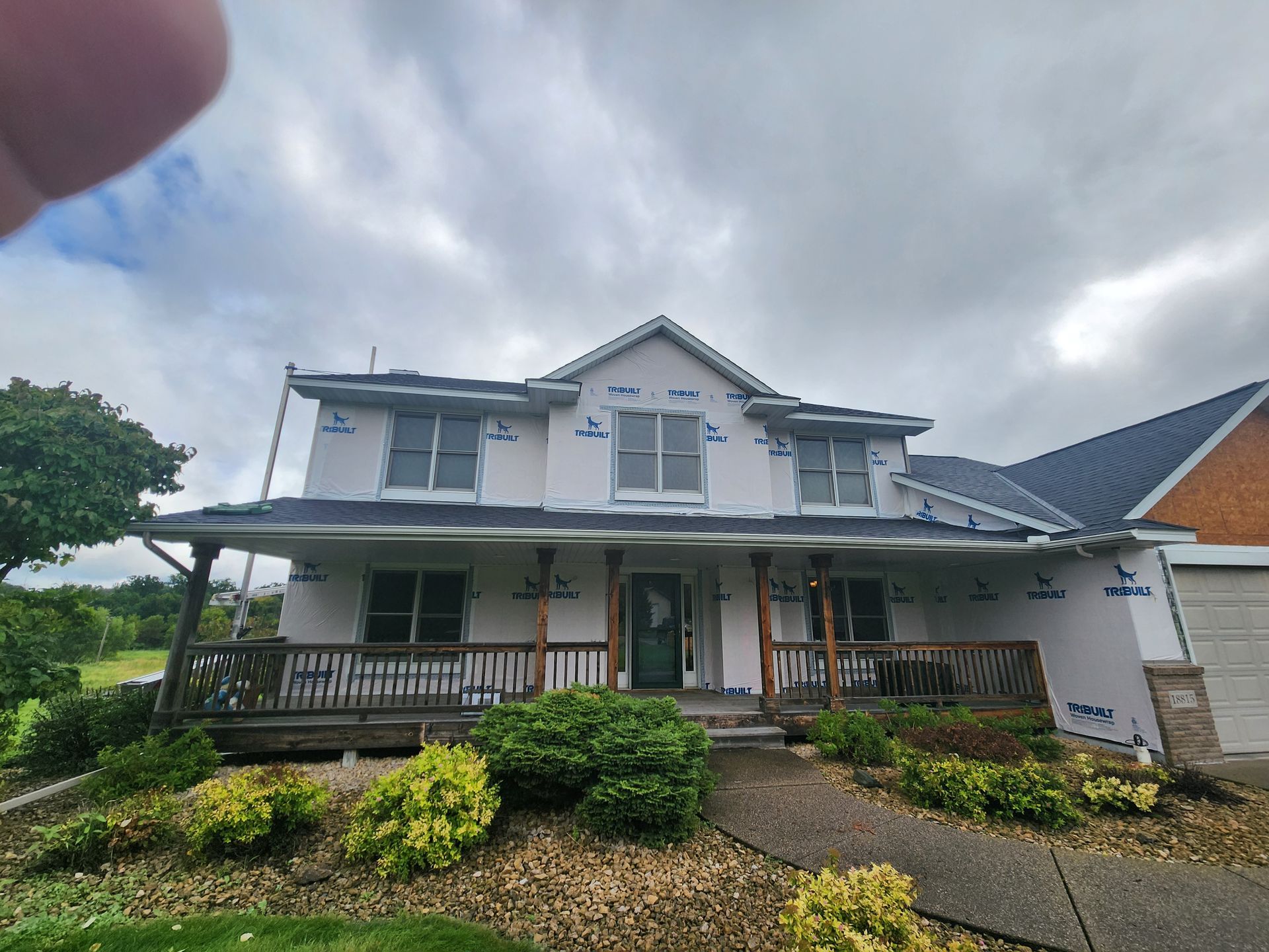 A white house with a green porch and a brick building in the background.