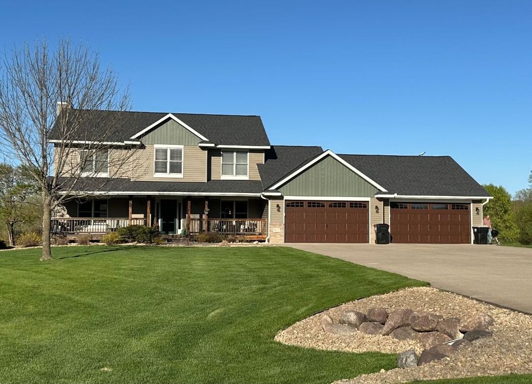 A large house with three garage doors and a large lawn in front of it.