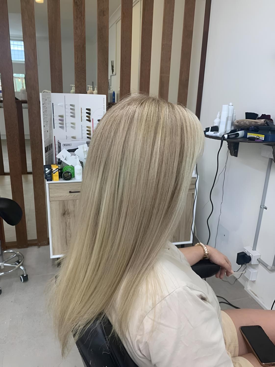 A Woman With Long Blonde Hair is Sitting in a Chair in a Salon — Dudes n Dolls Hair Lounge In Warners Bay, NSW