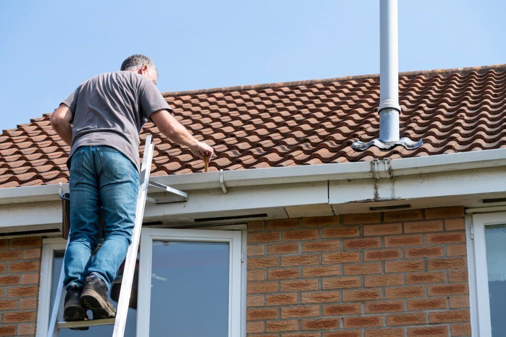 A man is standing on a ladder on the roof of a house.