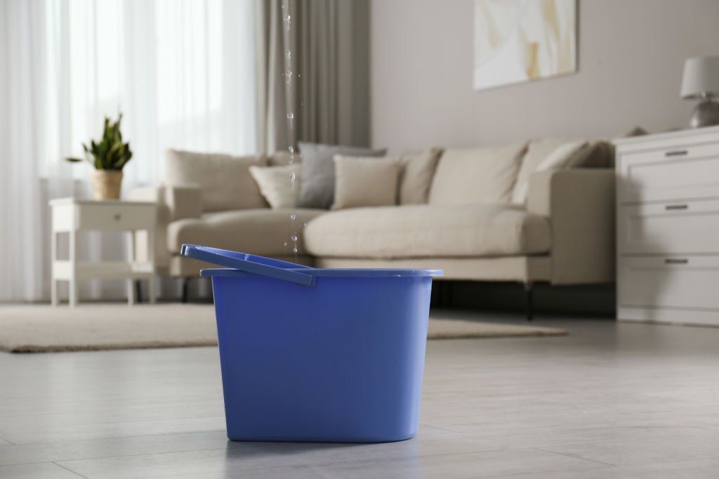 A blue bucket is sitting on the floor in a living room.