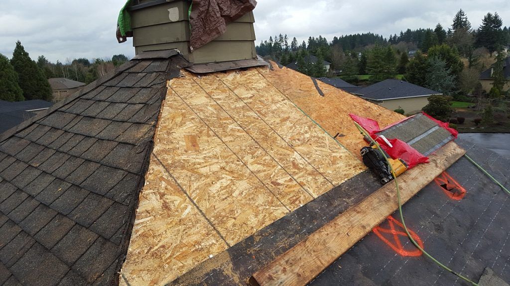 A roof with a chimney on top of it is being repaired.