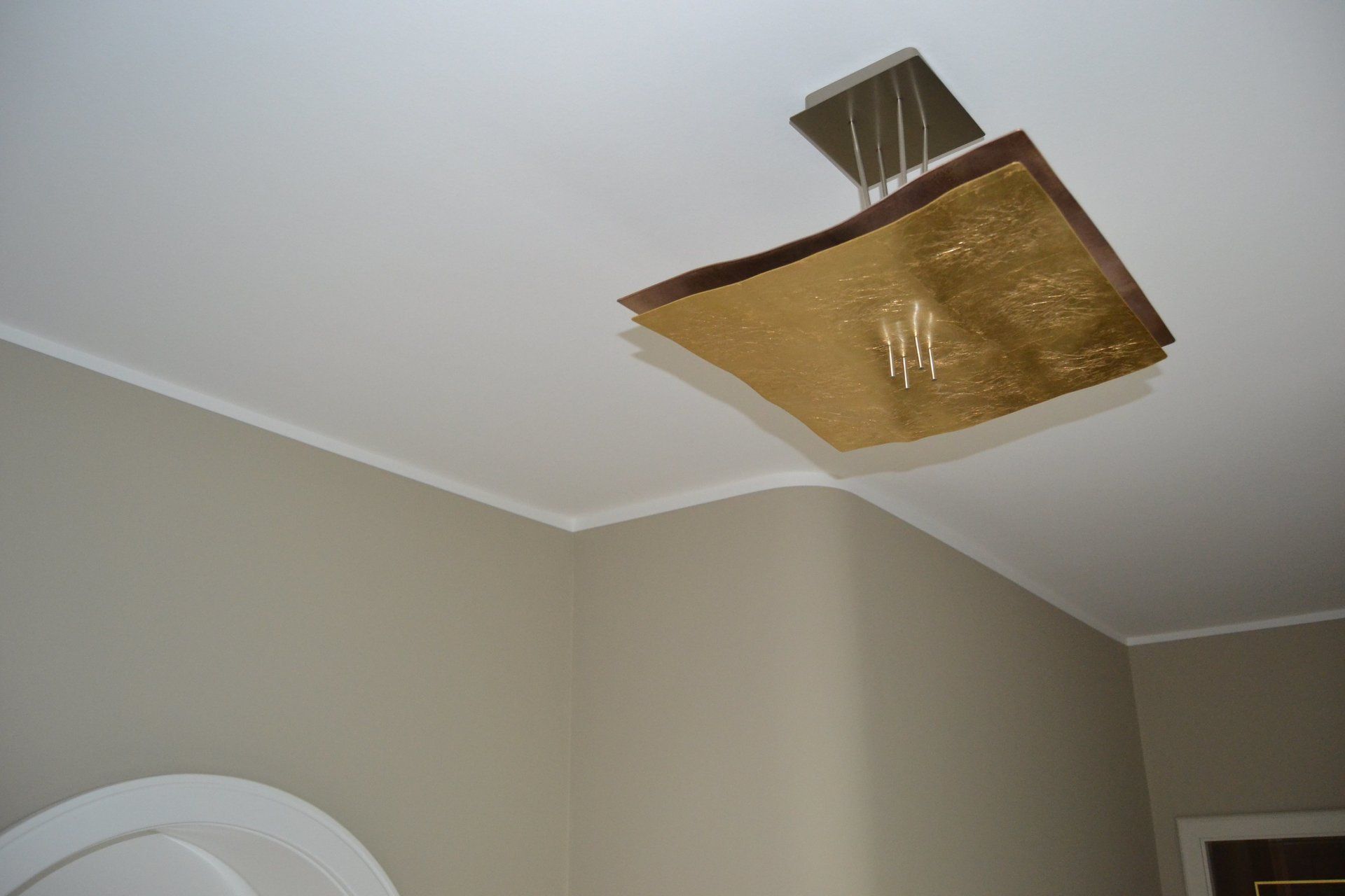 Beige gestrichene Wand und goldene Lampe an Decke