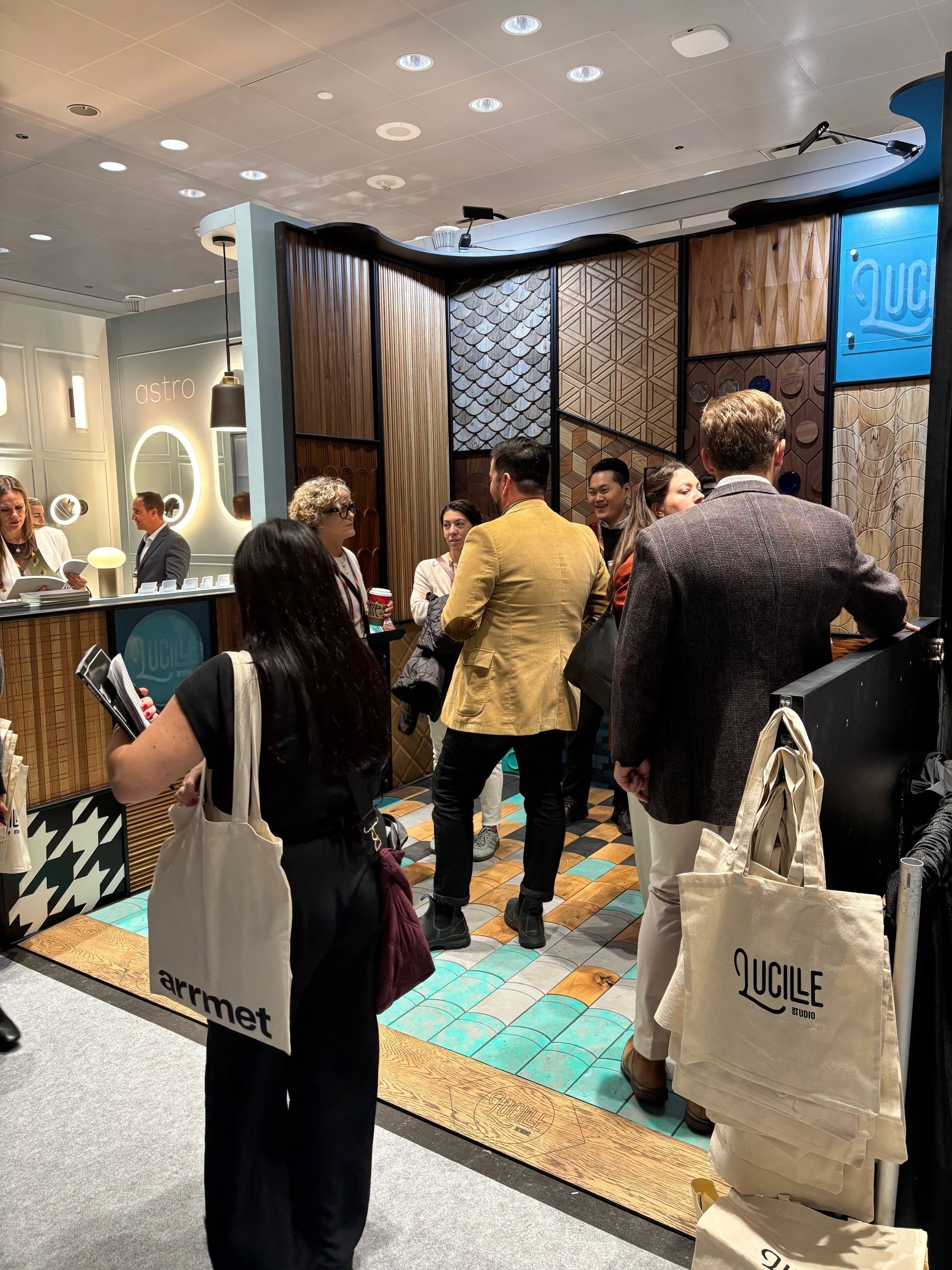 People at an interior design trade show. Display of wood panel samples. Attendees in the room, some holding tote bags.