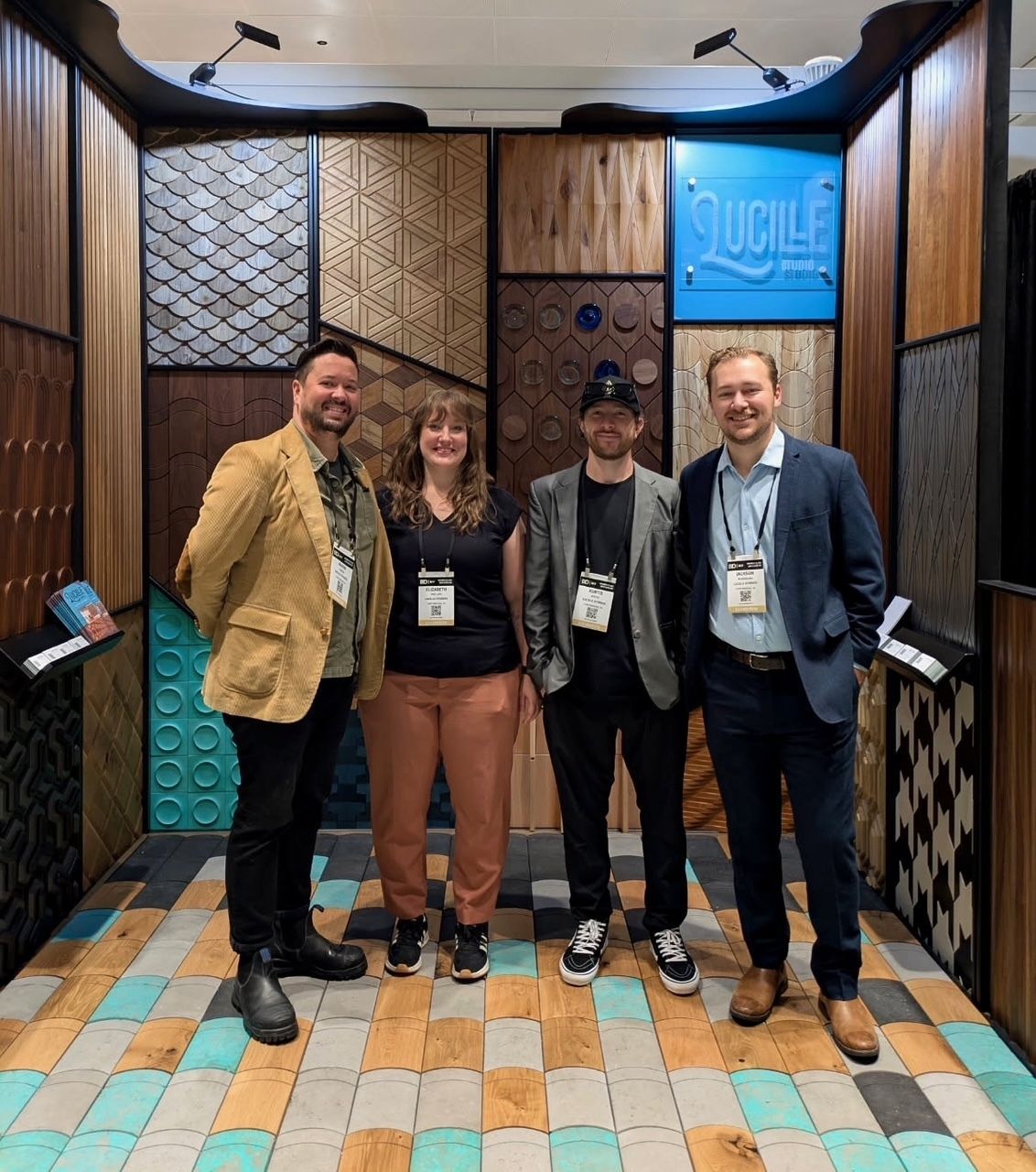 Four people pose in front of a wood-paneled display with various textures and colors.
