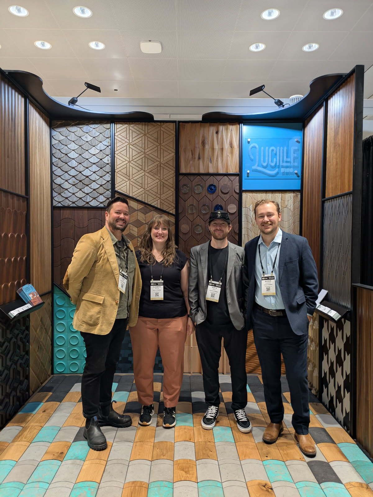 Four people stand in front of a display wall of wood panels at a trade show.