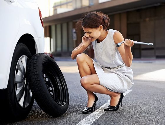Lady on her cell phone calling for help to change a flat tire