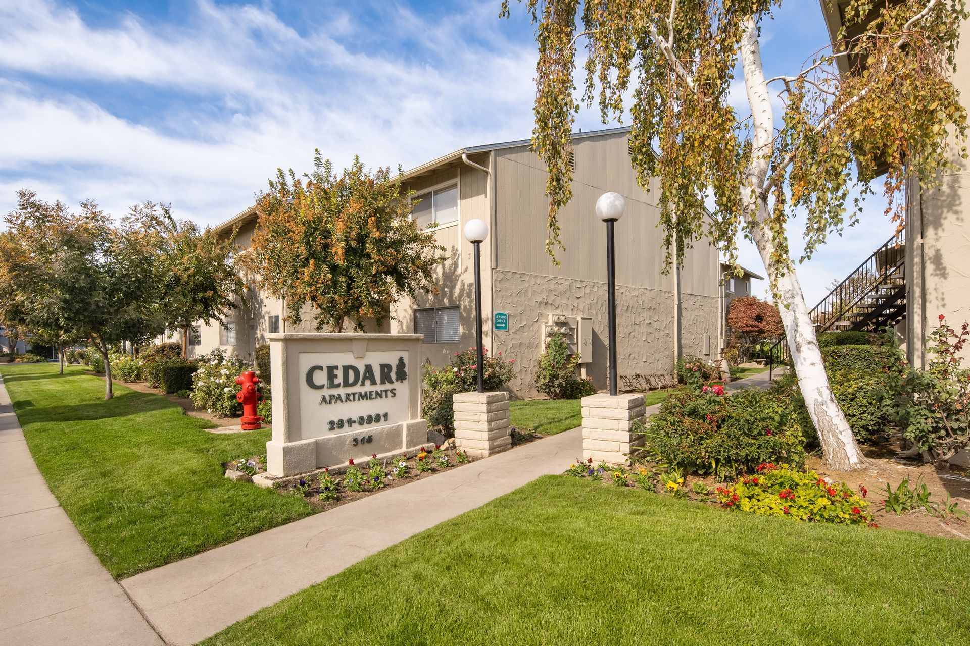 Cedar Apartments sign in front of a two-story beige building with green lawn and trees.