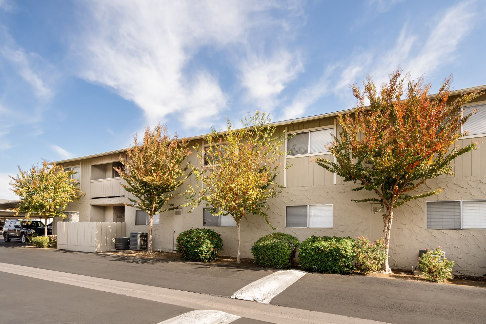 Apartment building with beige walls, trees with colorful foliage, and a blue sky.