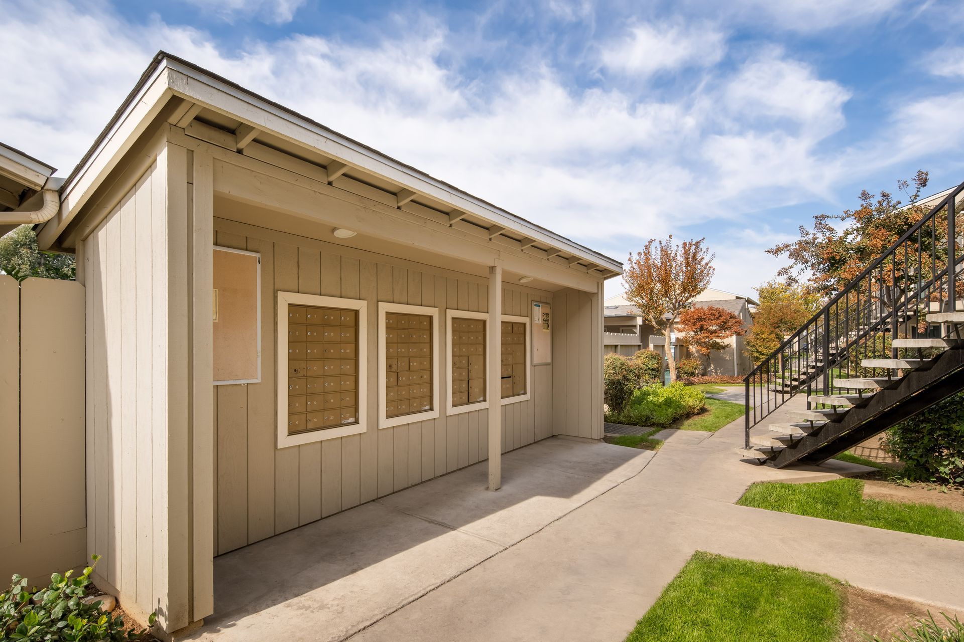 Beige building with boarded windows, concrete path, and metal staircase under a blue sky.