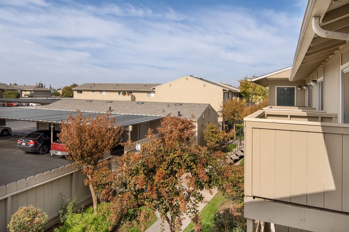 Apartment complex with tan buildings, covered parking, and trees under a blue sky.