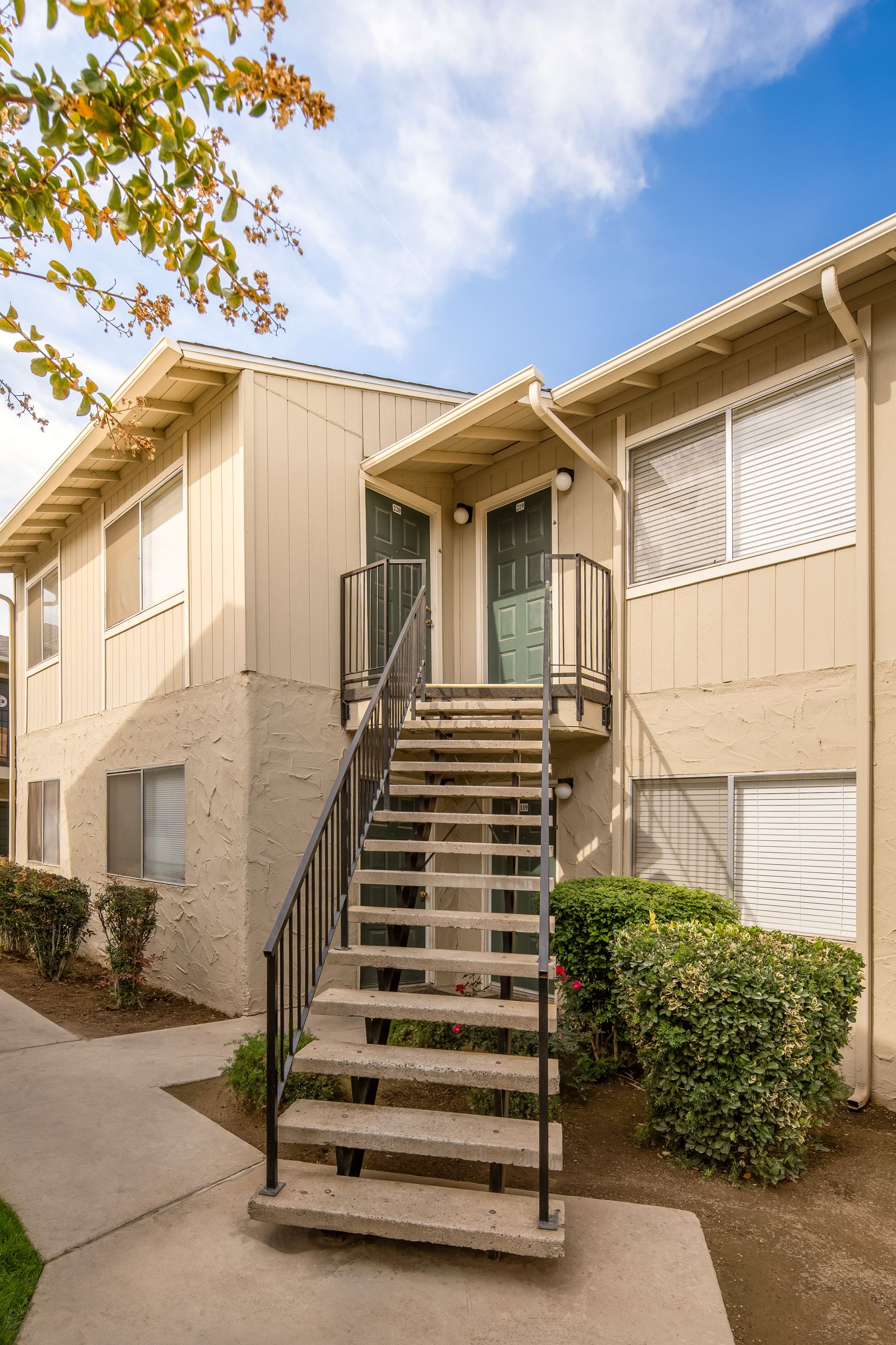 Two-story apartment building with exterior staircase. Tan and cream exterior with blue sky.