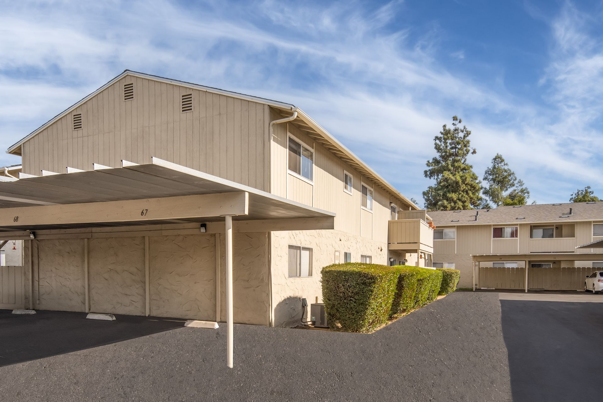 Apartment complex with tan buildings, carport, and asphalt driveway under a blue sky.