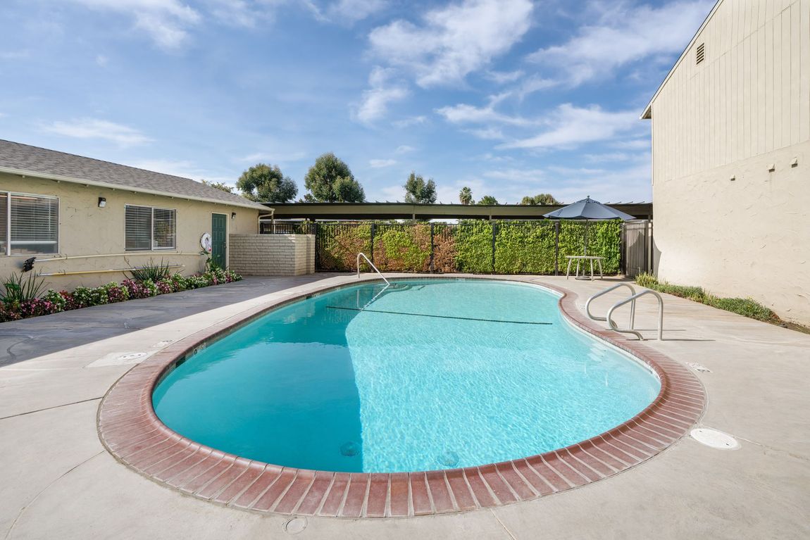 Swimming pool with turquoise water, surrounded by a brick border and concrete. Buildings on either side.
