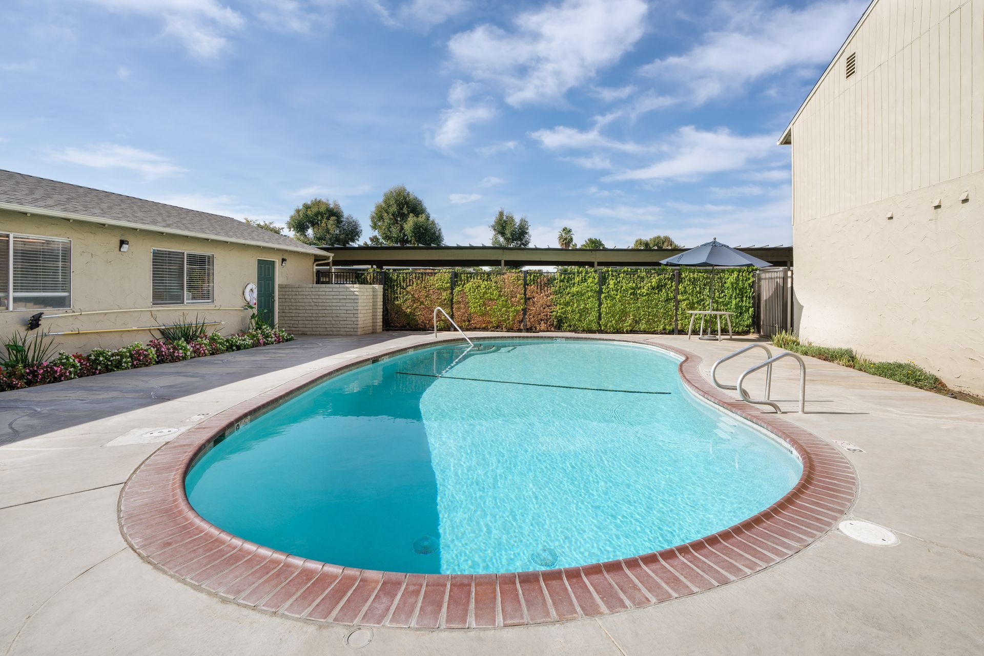 Swimming pool with turquoise water, surrounded by a brick border and concrete. Buildings on either side.